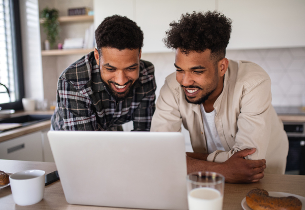 Portrait of young student brothers in kitchen indoors at home, using laptop.