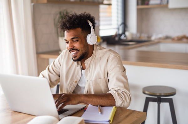 Portrait of young man student with laptop and headphones indoors at home, studying.