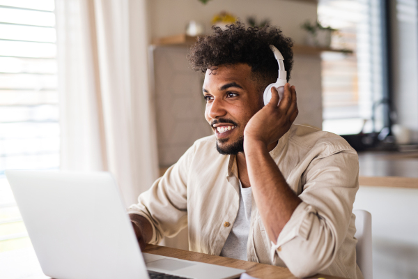 Portrait of young man student with laptop and headphones indoors at home, studying.