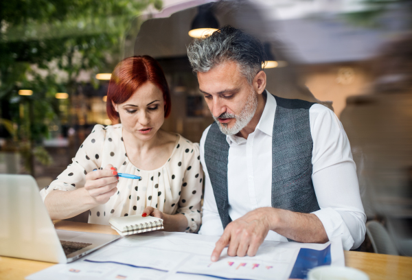 A man and woman having business meeting in a cafe, using laptop and smartphone. Shot through glass.