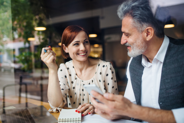 A man and woman having business meeting in a cafe, using laptop and smartphone. Shot through glass.