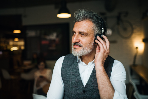 Mature man with headphones at the table in a cafe, listening to music.