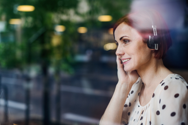 A portrait of woman with headphones sitting at the table in a cafe. Shot through glass.
