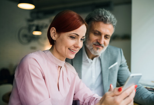 A man and woman having business meeting in a cafe, using smartphone.