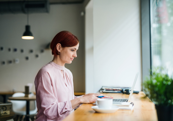 A portrait of attractive woman with coffee sitting at the table in a cafe, using laptop.