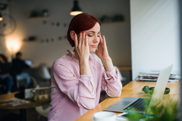 An attractive woman with laptop sitting at the table in a cafe, suffering from headache.
