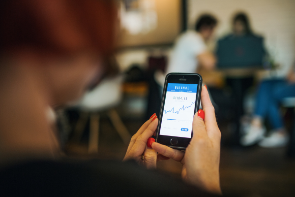 Midsection of unrecognizable woman with smartphone in a cafe, checking finances.
