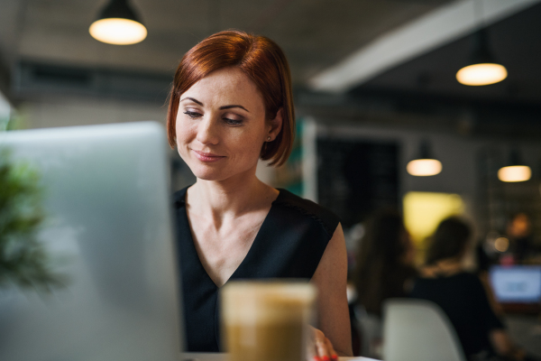 A portrait of attractive woman with coffee sitting at the table in a cafe, using laptop.