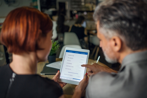 A rear view of man and woman having business meeting in a cafe, using tablet.