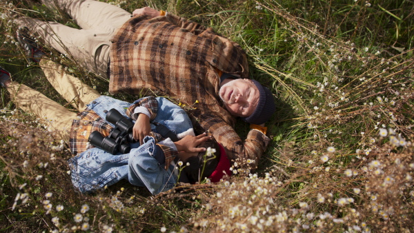 Grandfather lying in grass with his grandson, observing nature trough binoculars. Autumn season.