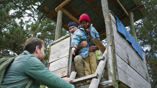 Grandfather, father and son having men time together in forest, climbing at high hunter seat, during autumn day.