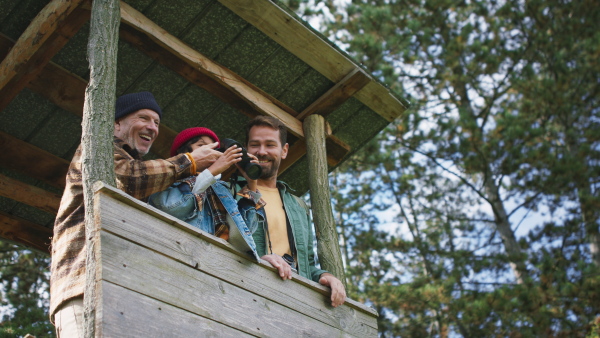 Grandfather, father and son having men time together in forest, sitting at high hunter seat drinking hot tea and observing nature.