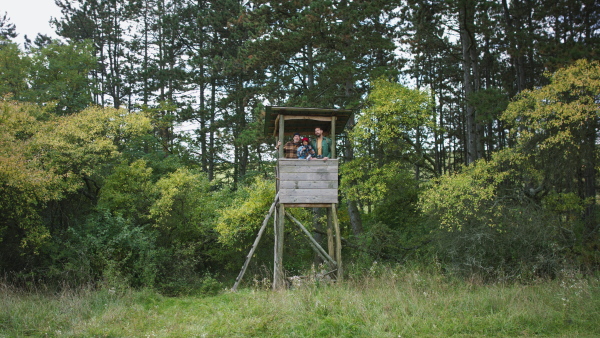 High hunter seat in forest with three generation of men, observing the nature trough binoculars.