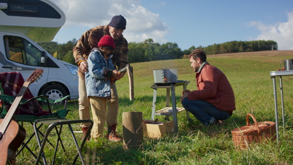 Grandfather, father and grandson preparing for outdoor barbecue in the nature, chopping wood and making fire. During autumn season.