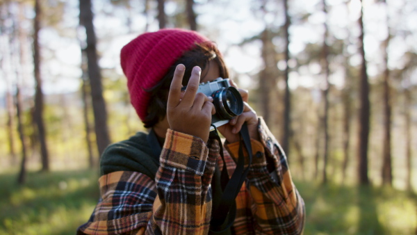 Little multiracial boy taking photos at old camera in the middle of forest in autumn season.