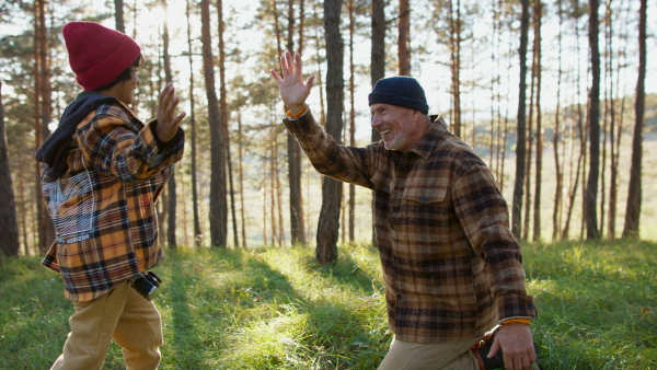 Grandfather with his grandson giving five in the forest, during autumn sunny day.