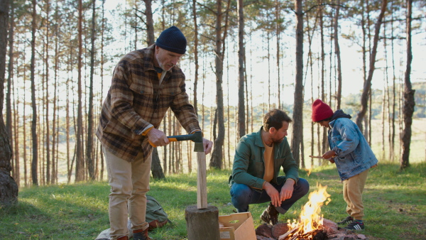 Three generations of men making fire in the autumn wildness forest, spending time together, observing nature.