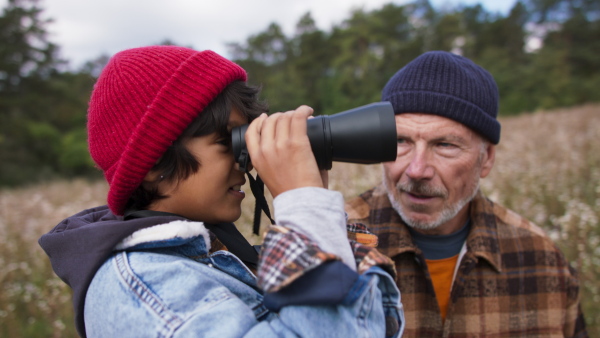 Senior man with his little grandson resting and looking trough binoculars,at autumn meadow during camping.