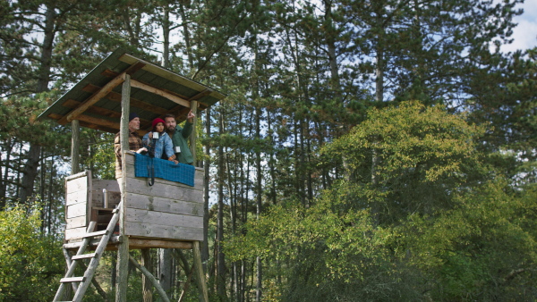 Grandfather, father and son having men time together in forest, sitting at high hunter seat drinking hot tea and observing nature.