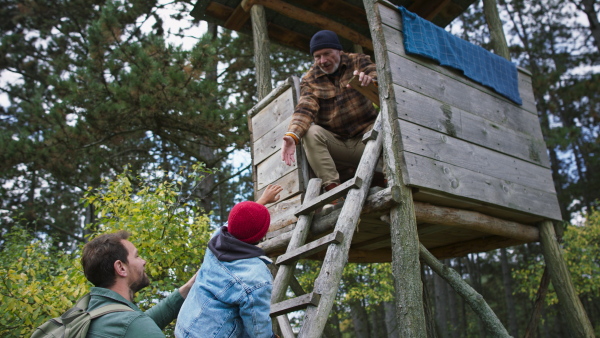 Grandfather, father and son having men time together in forest, sitting at a high hunter seat, climbing up.