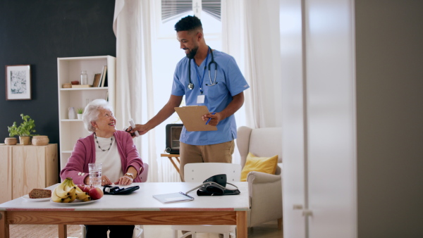 A happy healthcare worker or caregiver visiting senior woman indoors at home, talking.