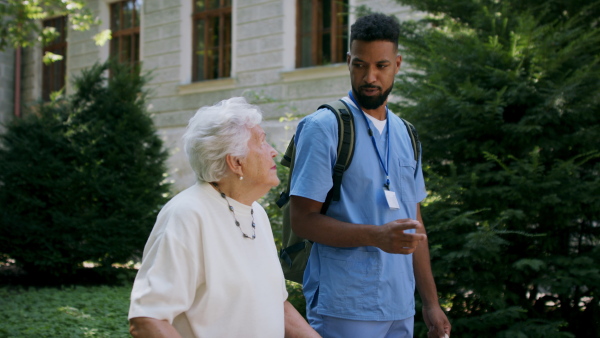 A senior woman and caregiver outdoors on a walk with walker in park, talking.