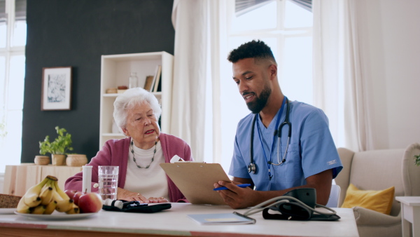 A happy healthcare worker or caregiver visiting senior woman indoors at home, talking and explaining dosage of pills.