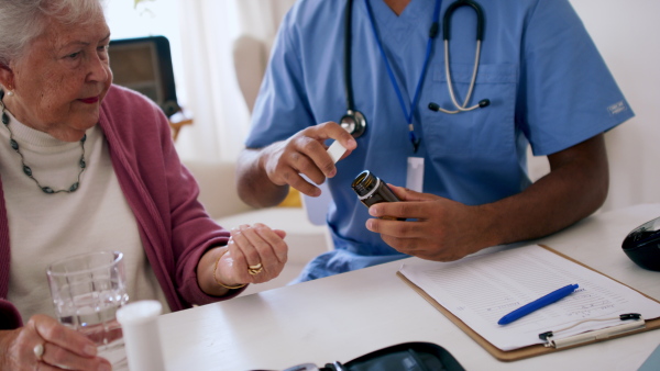 Close up of male healthcare worker or caregiver hand giving pills to senior woman indoors during home visit.