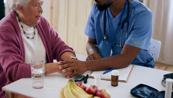 A close up of healthcare worker or caregiver visiting senior woman indoors at home, talking and cosoling.