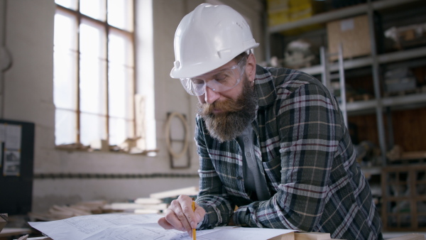 A male carpenter in protective goggles and helmet sketching desing of his product, looking at camera. Small business concept.