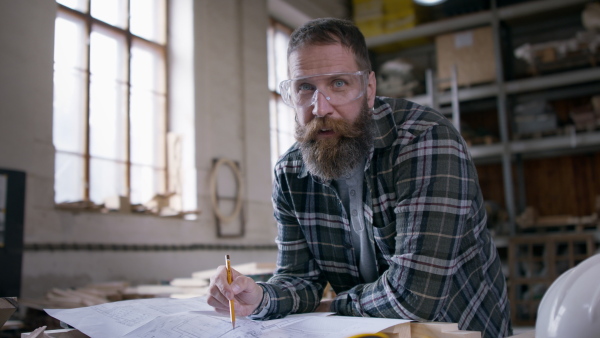 A male carpenter sketching desing of his product, looking at camera. Small business concept.