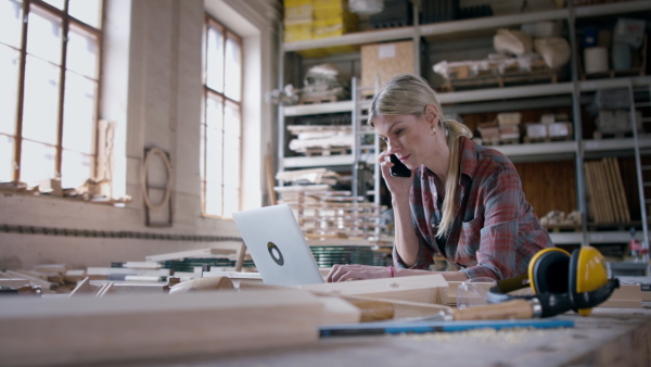 A female carpenter with smartphone and laptop working on her product. Small business concept.