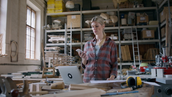 A female carpenter with smartphone and laptop working on her product. Small business concept.