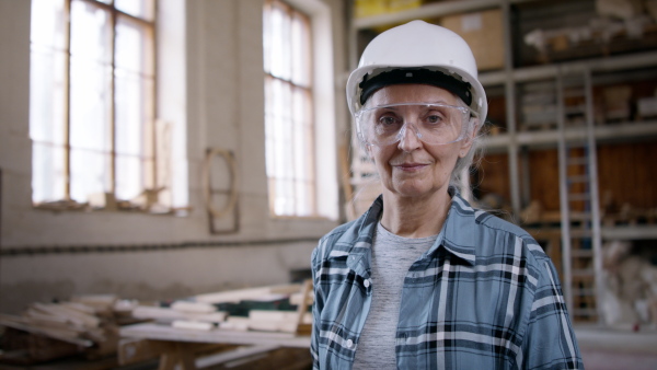 A senior female carpenter standing in workshop and looking at camera. Small business concept.