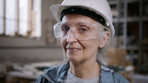 A headshot of senior female carpenter standing in workshop and looking at camera. Small business concept.