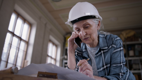 A senior female carpenter having a call and sketching design of her product. Small business concept.