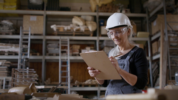 A senior female carpenter sketching design of her product and looking at camera. Small business concept.