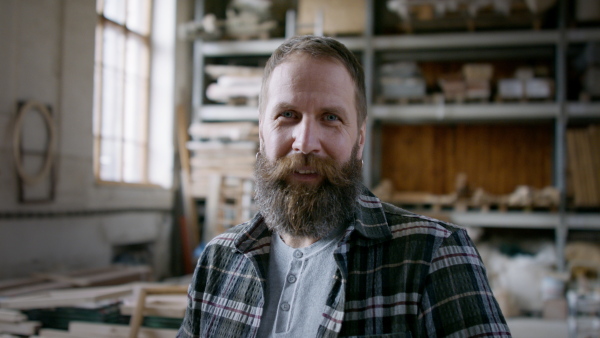 A male carpenter standing in workshop and looking at camera. Small business concept.