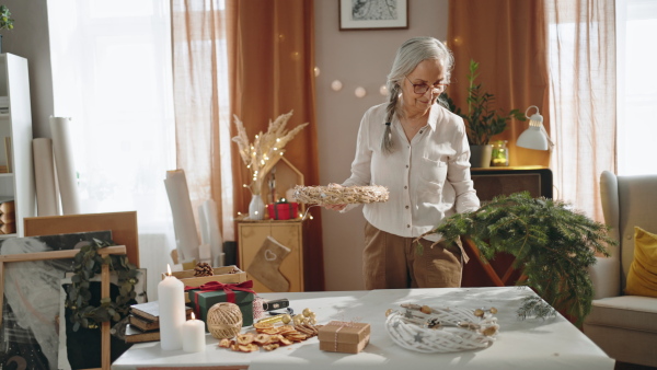 Senior woman a making Christmas wreath from natural materials indoors at home