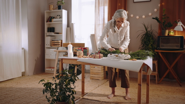 Senior woman a making Christmas wreath from natural materials indoors at home