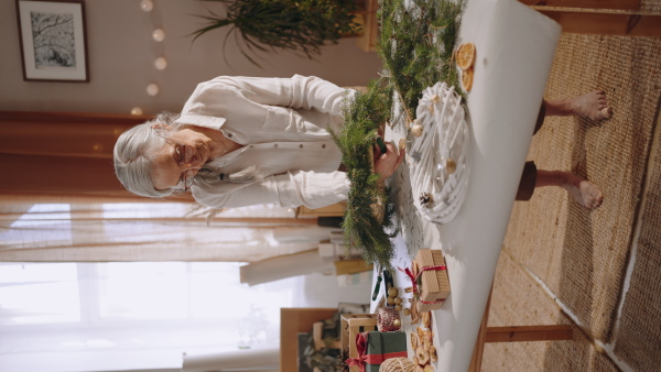 A vertical footage of senior woman making Christmas wreath from natural materials indoors at home