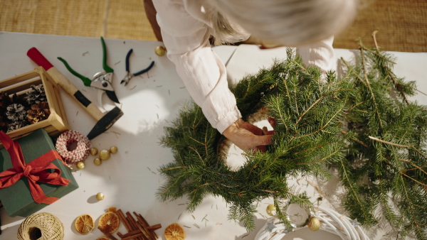 A top view of senior woman making Christmas wreath from natural materials indoors at home