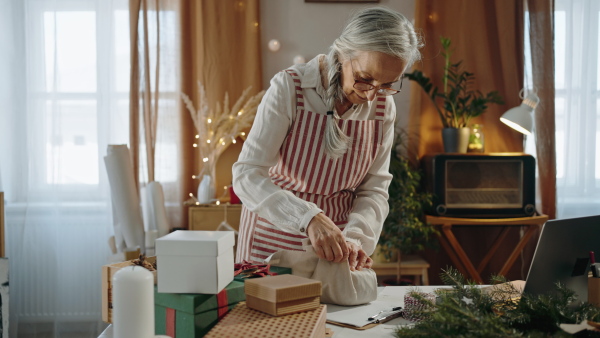 A senior woman packing Christmas present in natural materials indoors at home, environmental gift wrapping concept