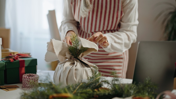 A close up of senior woman wrapping Christmas present in natural materials indoors at home, environmental gift wrapping concept