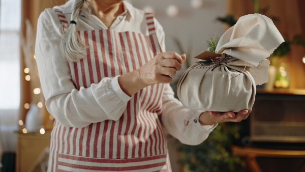 A close up of senior woman wrapping Christmas present in natural materials indoors at home, environmental gift wrapping concept