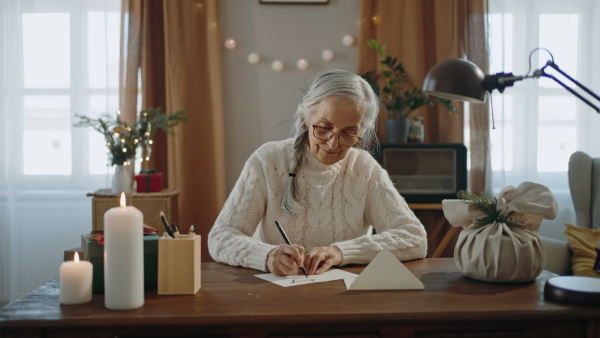 A happy senior woman writing Christmas cards indoors at home.