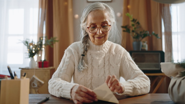 A happy senior woman writing Christmas cards indoors at home, looking at camera.