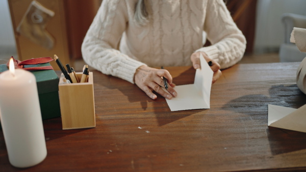 A senior woman writing Christmas cards indoors at home, looking at camera.