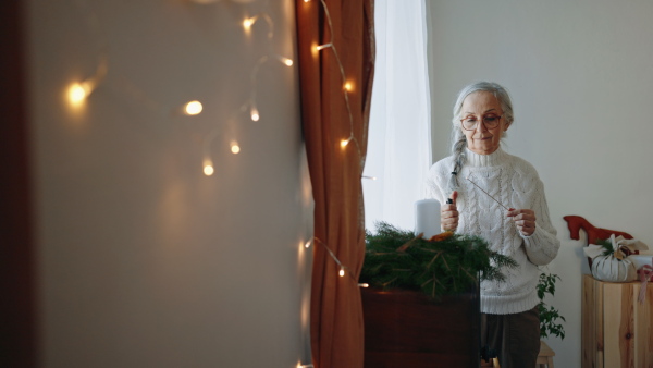 A senior woman lighting up candle at Christmas wreath indoors at home.