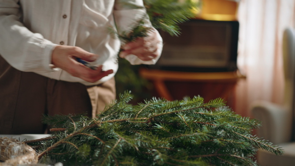 An unrecognizable senior woman cutting branch to make Christmas wreath indoors at home